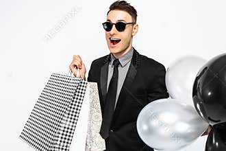 An excited guy in a black suit and sunglasses, with shopping bag