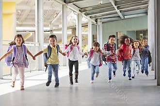 Primary school kids run holding hands in corridor, close up