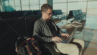 Alone male passenger is waiting his flight in a terminal and browsing in laptop