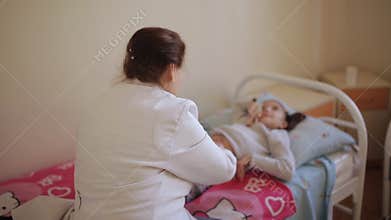 The elderly woman masseur doing massage of the abdomen to the little girl in the hospital.