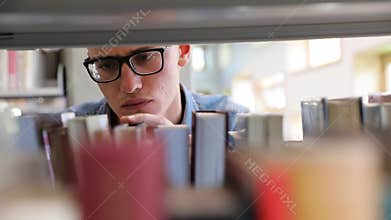 Man Looking For Book On Bookshelves At Library At College