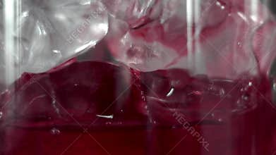 Macro shoot of Red martini pouring in a glass full with a ice cubes. Martini fill a glass with ice. Making of cocktails
