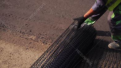 Worker rolls the mesh on the road before laying the asphalt