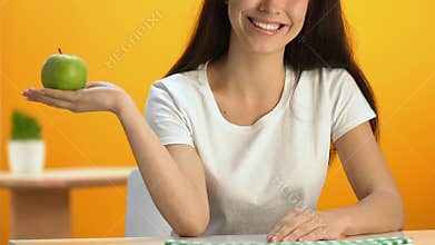 Happy woman demonstrating fresh green apple and smiling into camera, dieting