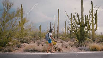 Slow motion wide shot, happy young adult tourist woman walking along amazing wild cactus desert road in national park.