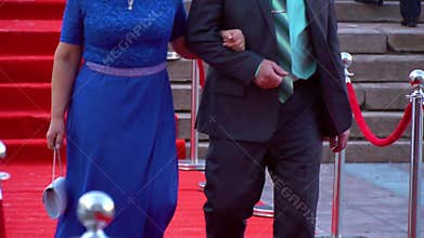 A woman in a blue dress is walking alongside a man in a formal suit, on the red carpet