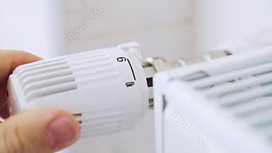A man regulates the temperature in the house with a thermostat on the radiator