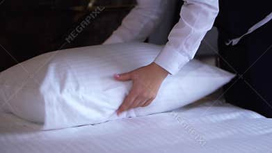 A hotel cleaning lady straightens a pillow in a small, cozy hotel room.