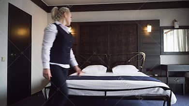 Maid makes a double bed and straightens the pillow in a small, cozy hotel room.