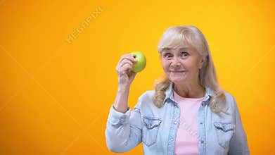 Optimistic elderly lady biting fresh green apple, healthy teeth, stomatology