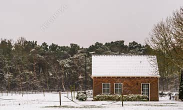 Small farmers cottage in a winter landscape scenery, farm fields and house covered in snow, living near the forest