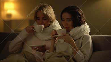Two ill women drinking hot tea and smiling, feeling better after treatment