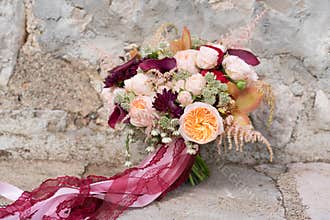 Peach dark red wedding bouquet stands on a stone wall background