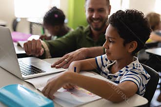 Young school teacher helping boy with study on laptop in classroom