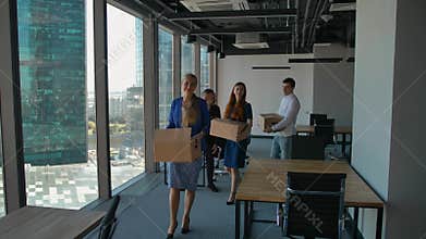 Happy businesspeople walk in new office, with boxes, smiling.