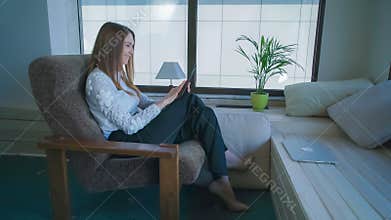Adult woman at home using touch screen tablet and smiling.