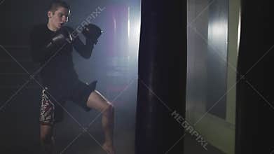 Muay thai fighter punching in smoky studio. Kickboxer training with punching bag