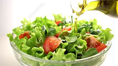Bottle of olive oil pouring over mixed salad.