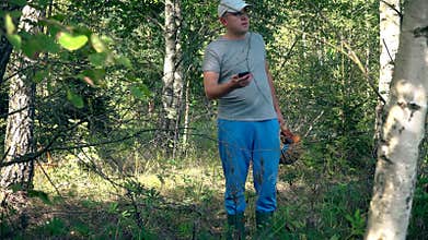 Man with full basket of mushrooms looking for his GPS signal on smartphone