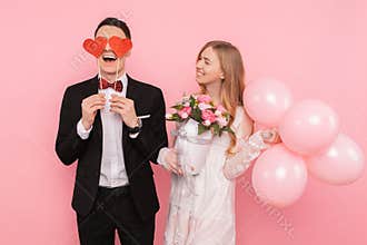 A loving couple, a man holding two paper hearts in his eyes, and a woman holding a bouquet of flowers, on a pink background