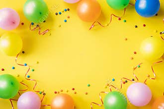 Heap of colorful balloons, confetti and candies on yellow table top view. Birthday party background. Festive greeting card
