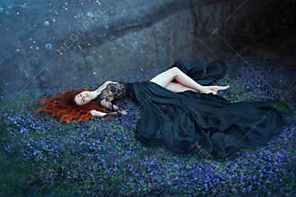 Girl with red hair lying on grass in dark forest, black queen lost in battle, charming lady in long black royal dress