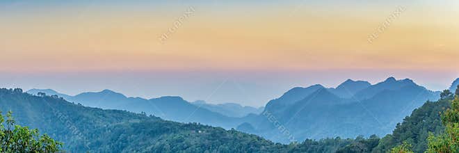 Nature Web Banner. Mountain view sunset panorama view of many hill and green forest cover with soft mist with colorful sky