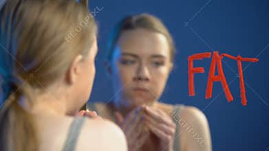 Young woman chewing donut, wiping word fat mirror glass, eating disorder, health