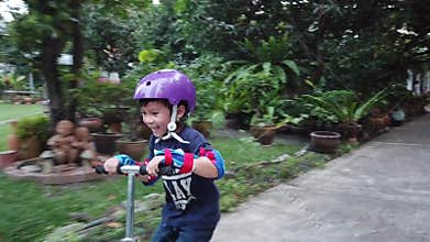 Little kid is learning to ride a scooter with full protection