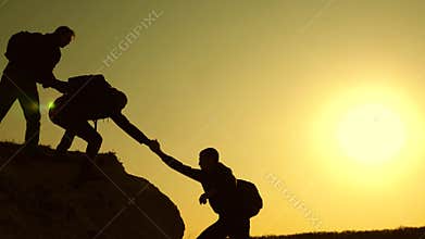 Climbers silhouettes stretch their hands to each other, climbing to the top of the hill. travelers climb one after