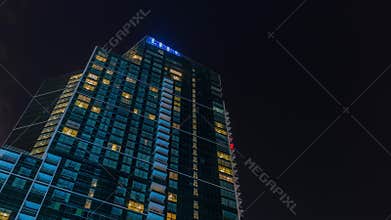 Night Sky with clouds above modern skyscraper with glowing windows architecture timelapse.