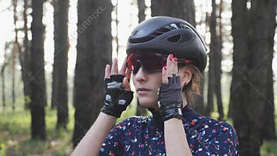 Portrait of young attractive girl putting glasses on before cycling wearing black helmet and blue jersey. Cycling Concept. Slow mo