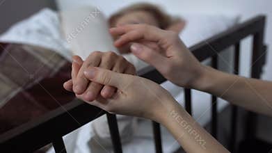 Daughter supporting her terminally ill mother lying on hospital bed, hospice