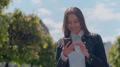 Attractive young woman at the sunny city streets and chatting with friends, joyful hipster girl using cellphone outdoors