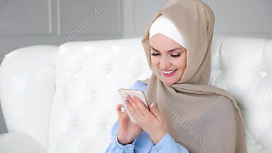 Muslim woman in hijab is chatting in smartphone and laughing.