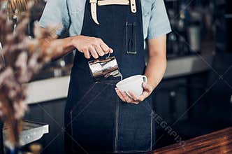 Man barista pour milk into hot coffee cup at counter bar in front of machine in cafe restaurant,Food business owner concept