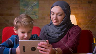 Portrait of small boy and his muslim mother in hijab watching into tablet together and discussing.