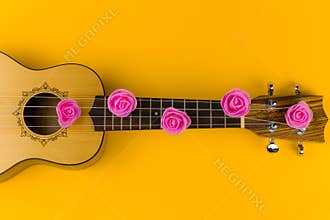 guitar with rose flowers on the strings lies on vibrant yellow background