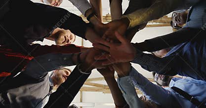 Close-up happy diverse adult business people joining hands together. Team spirit at modern multiethnic loft office.