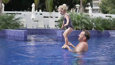 Dad plays with his little daughter in the outdoor pool