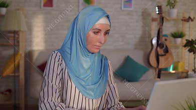 Portrait young muslim woman in a hijab with a scar from a burn on her face works at a laptop