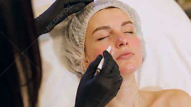 Beautician draws the contours of a white pencil on the face of the patient.
