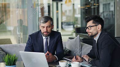 Mature businessmen talking in cafe looking at laptop screen discussing contract