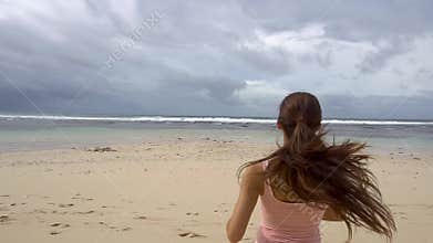 Woman running to sea water and raise arms enjoying freedom on beach at sunrise