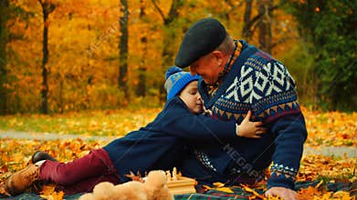Little boy is hugging his grandfather are sitting in the autumn park