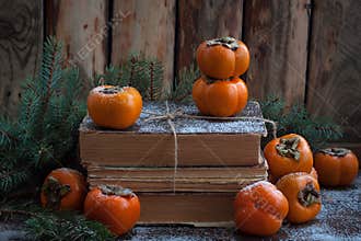 Persimmon on the pack of old books on the wooden background with branches of fir tree