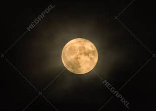 Glowing yellow full winter moon with illuminated clouds
