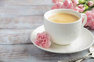 Cup of fresh morning coffee with pink carnation flowers on a wooden background. Valentine`s day concept.