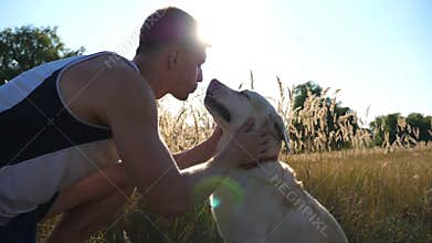 Young man caress, hugging and kissing his labrador outdoor at nature. Playing with golden retriever. Dog licking male