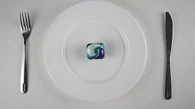 Washing powder pod on a plate, detergent pod. Zoom in. Preparing to eat a capsule with detergent, washing powder pods